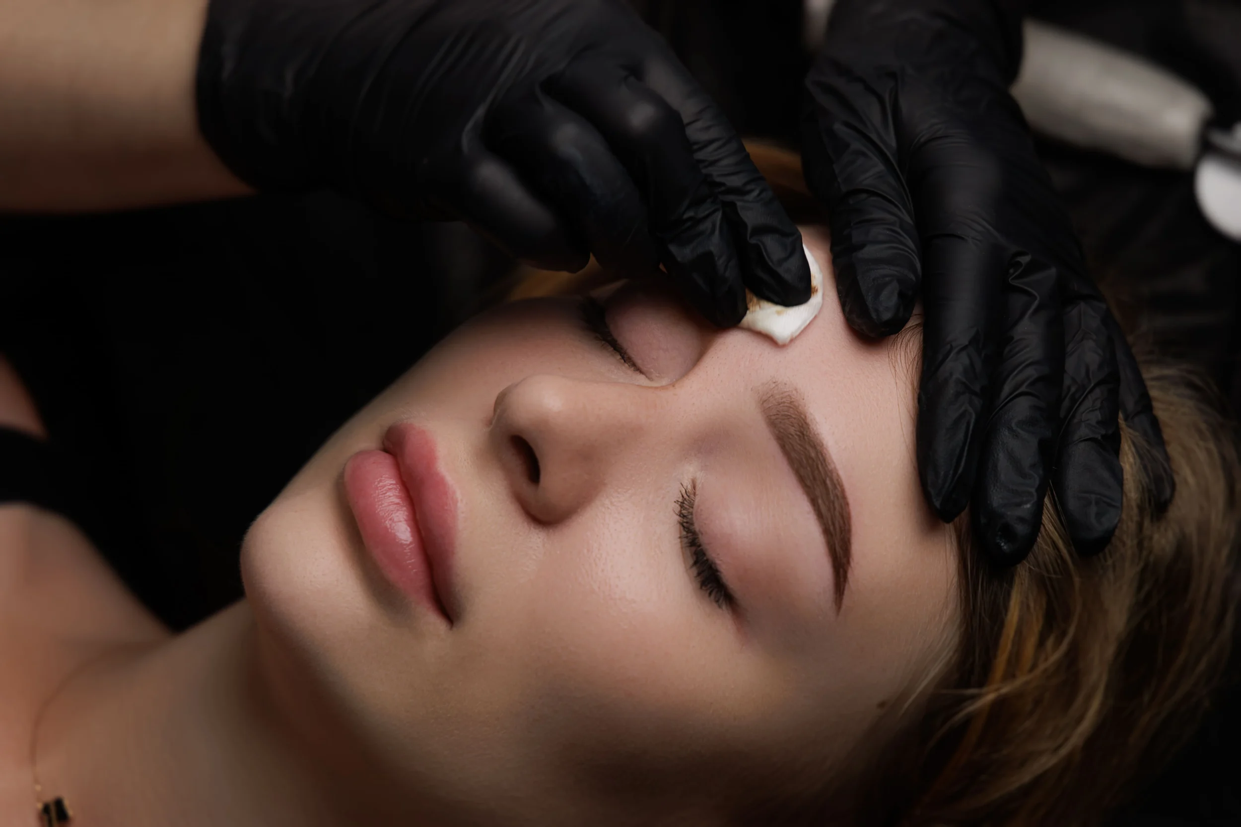 A gloved technician carefully shaping a clients brows during a natural eyebrow waxing service at a professional beauty studio