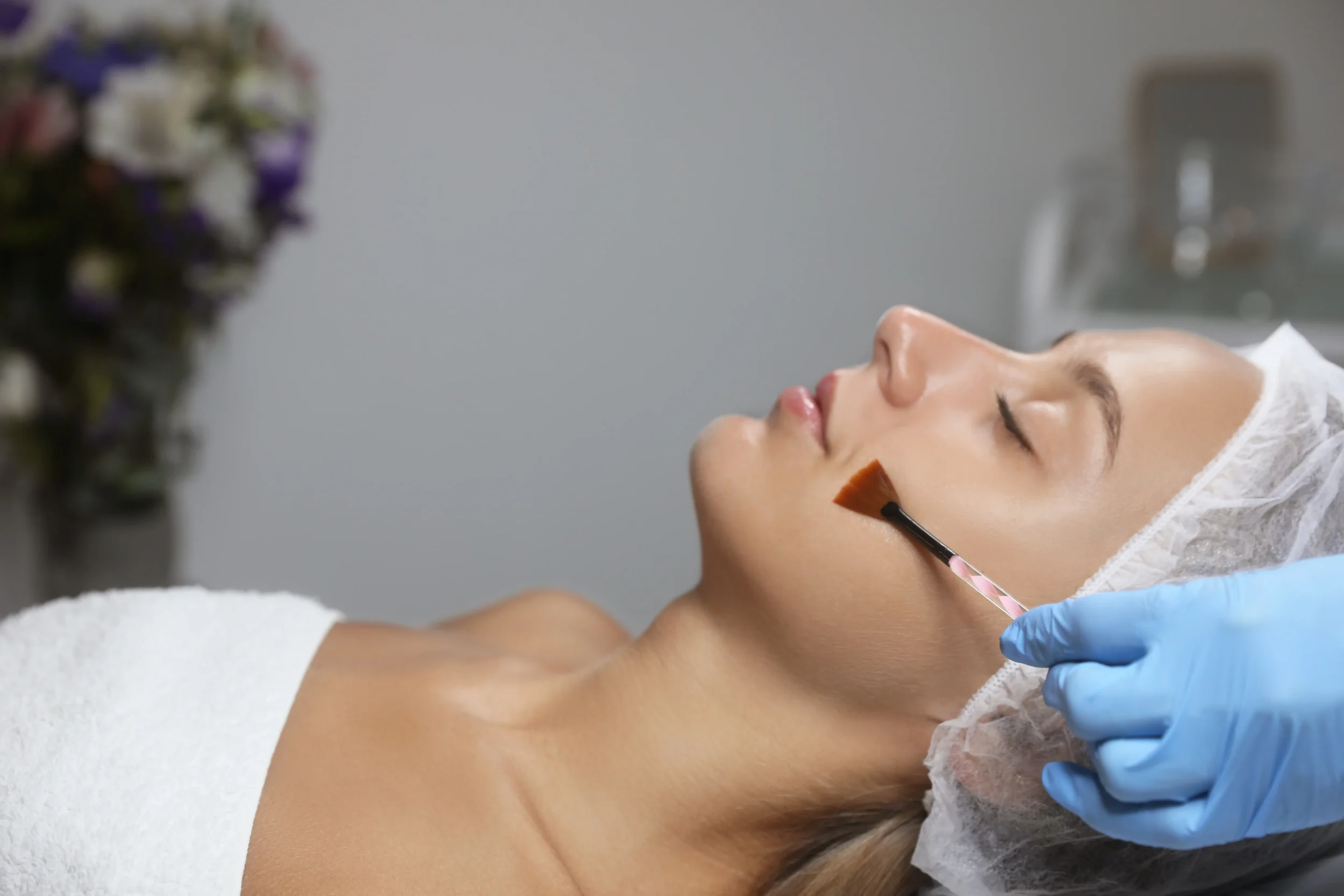 A licensed esthetician applying a chemical peel treatment to a clients face using a brush in a professional spa setting 3