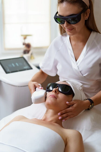 technician performing a photorejuvenation laser treatment on a client wearing protective goggles to repair treatment for sun damaged skin in a professional clinic